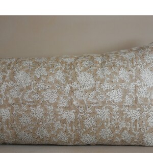 Puede incluir: Una almohada larga y rectangular con una funda de tela de lino beige. La almohada tiene un patr&oacute;n floral blanco con un dise&ntilde;o repetitivo de peque&ntilde;as flores y hojas.