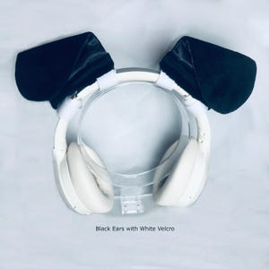 K&ouml;nnte beinhalten: Cremefarbene Over-Ear-Kopfh&ouml;rer mit zwei gro&szlig;en, pl&uuml;schigen schwarzen Ohren, die mit wei&szlig;en Klettverschl&uuml;ssen am Kopfb&uuml;gel befestigt sind. Der Text "Black Ears with White Velcro" ist unten im Bild mittig unter dem Kopfh&ouml;rer aufgedruckt.