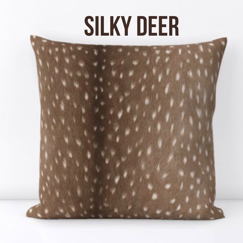 Może przedstawiać: Kwadratowa poduszka z brązowym wzorem i białymi plamkami, przypominająca sierść jelenia. Tekst "SILKY DEER" jest wydrukowany ciemnobrązowym kolorem u g&oacute;ry. Jest to element wystroju domu.