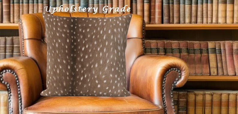 Może przedstawiać: Kwadratowa poduszka dekoracyjna z brązowo-białym wzorem w plamki, oznaczona jako "Upholstery Grade". Poduszka umieszczona jest na brązowym sk&oacute;rzanym fotelu przed p&oacute;łką z książkami. Wz&oacute;r poduszki przypomina sierść zwierzęcia.
