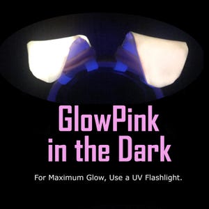 K&ouml;nnte beinhalten: Ein Haarreif mit zwei aufrechten, leuchtend wei&szlig;en Tierohren vor schwarzem Hintergrund. Der Text lautet: GlowPink in the Dark. For Maximum Glow, Use a UV Flashlight. Die Ohren strahlen helles Licht aus, w&auml;hrend der Haarreif dunkel ist.