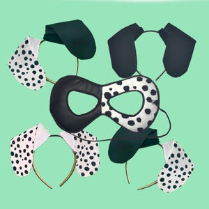 May include: A set of Dalmatian-themed costume accessories, including a black and white spotted eye mask and matching ear headbands. The ears are white with black spots, and the mask is half black and half white with spots. The background is a light green.