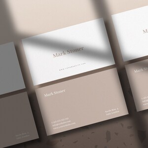 May include: Five white business cards with the name "Mark Stoner" printed on them. The cards are arranged in a staggered pattern on a brown and white speckled surface.