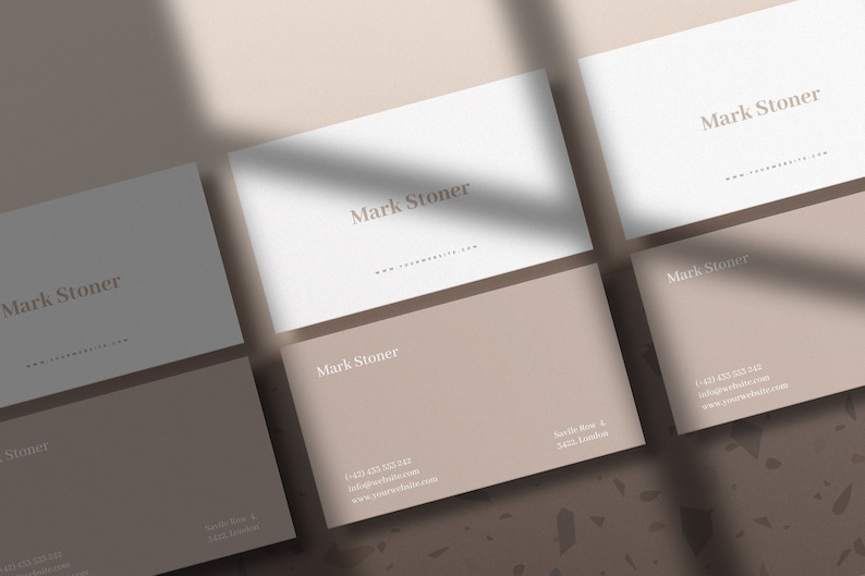 May include: Five white business cards with the name "Mark Stoner" printed on them. The cards are arranged in a staggered pattern on a brown and white speckled surface.