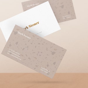 May include: Two business cards with a terrazzo pattern. The top card is white with gold lettering that reads "Mark Stoner". The bottom card has a light brown terrazzo pattern with white lettering that reads "Mark Stoner", a phone number, email address, website address, and the address "Savile Row 4, 3423 London."