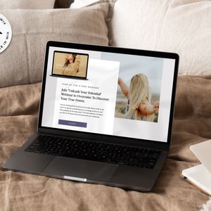 May include: A laptop computer on a bed with a brown blanket. The laptop screen shows a webpage with the text "Join 'Unleash Your Potential' Webinar to Overcome To Discover Your True Power."