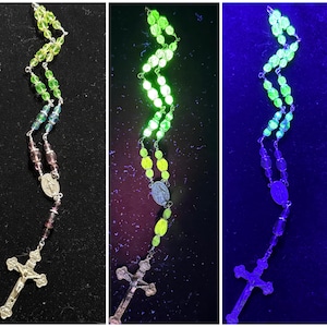 May include: A green glass rosary with a silver crucifix and a silver pendant of the Virgin Mary. The rosary glows under a blacklight.