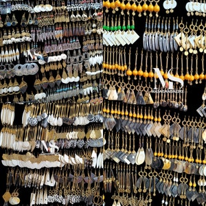 May include: A large collection of earrings made from various materials, including wood, bone, metal, and beads. The earrings are displayed on a black background and are arranged in rows. Some of the earrings are long and dangle, while others are short and stud-like. The earrings are all different colors and designs.