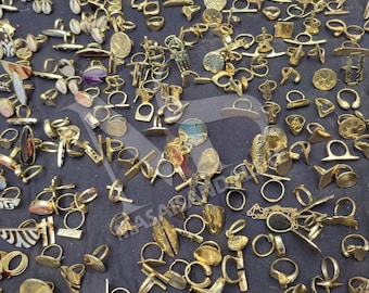 May include: A collection of gold-colored rings of various designs, including bands, signet rings, and rings with decorative elements. The rings are displayed on a dark surface, showcasing a variety of shapes and styles, suitable for different tastes and occasions.