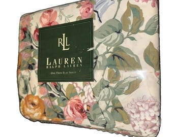 Op de afbeelding: Een verpakt Lauren Ralph Lauren eenpersoons laken met een crèmekleurige achtergrond en een bloemenpatroon van roze, gele en oranje rozen en groene bladeren. Een donkergroen label toont de tekst RLL Lauren Ralph Lauren.