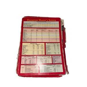 May include: A red Dungeon Master's Screen for a tabletop role-playing game, featuring a multi-panel design with printed reference tables, including character hit rolls, saving throws, missile fire, speed, encumbrance, and various experience tables.