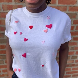 May include: A white t-shirt with pink and red embroidered hearts.