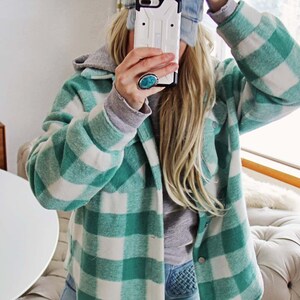 May include: A green and white checked flannel shirt with a hood. The shirt is worn over a grey hooded sweatshirt and blue jeans.