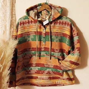 May include: A hooded sweatshirt with a colorful geometric pattern in shades of orange, red, green, and yellow. The sweatshirt has a single button closure at the neck and a kangaroo pocket.