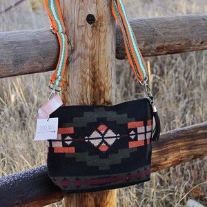 May include: A black shoulder bag with a geometric pattern in shades of orange, green, and white. The bag has a matching strap with orange, green, and white stripes. A black tassel hangs from the side. The tag reads "SPOOL No 72".