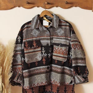 May include: A button-down shirt with a Southwestern-inspired pattern in shades of gray, black, and rust. The shirt has two front pockets and a collared neckline. The fabric appears to be a soft, woven material.