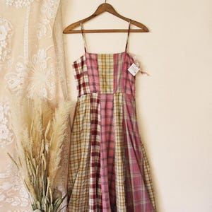 Puede incluir: Un vestido de patchwork con un estampado de cuadros rosa, rojo y beige. El vestido tiene tirantes finos y un escote recto.