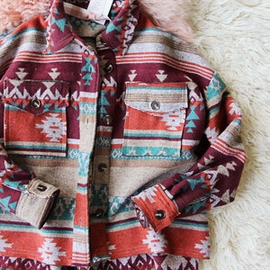 Peut inclure: Une chemise &agrave; manches longues boutonn&eacute;e avec un motif g&eacute;om&eacute;trique d'inspiration sud-ouest dans des tons de rouge, orange, turquoise et marron. La chemise a une coupe d&eacute;contract&eacute;e et un ourlet l&eacute;g&egrave;rement court.