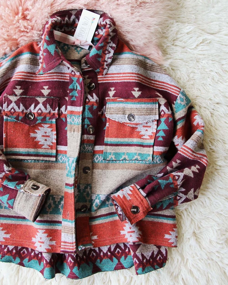 Peut inclure: Une chemise &agrave; manches longues boutonn&eacute;e avec un motif g&eacute;om&eacute;trique d'inspiration sud-ouest dans des tons de rouge, orange, turquoise et marron. La chemise a une coupe d&eacute;contract&eacute;e et un ourlet l&eacute;g&egrave;rement court.