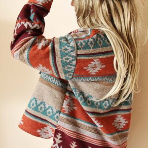 Peut inclure: Un cardigan &agrave; manches longues de couleur rouille avec un motif g&eacute;om&eacute;trique dans des tons de turquoise, marron et bordeaux. Le cardigan a un col ch&acirc;le et une coupe ample.