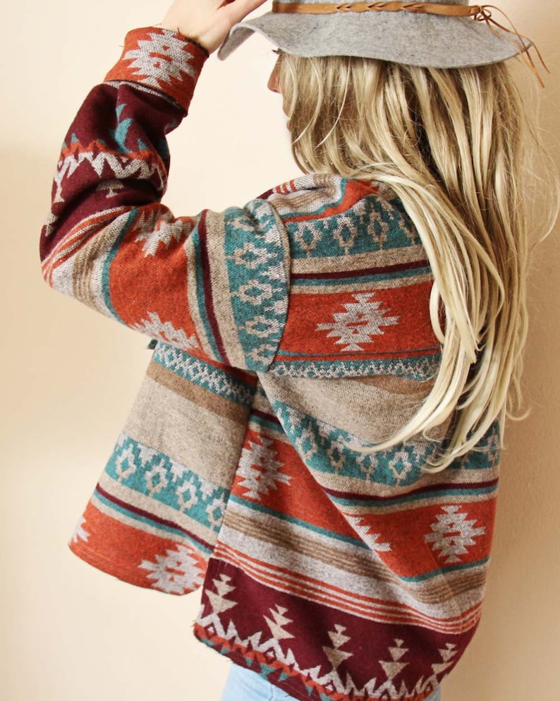 Peut inclure: Un cardigan &agrave; manches longues de couleur rouille avec un motif g&eacute;om&eacute;trique dans des tons de turquoise, marron et bordeaux. Le cardigan a un col ch&acirc;le et une coupe ample.