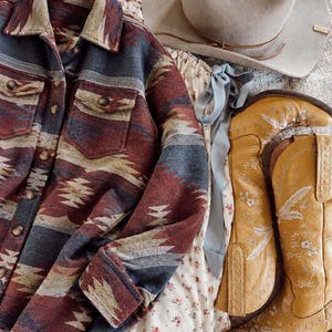 Könnte beinhalten: Ein langärmeliges Hemd mit Knopfleiste und einem mehrfarbigen geometrischen Muster in Rot-, Blau- und Beigetönen, ein hellbeiger Filzhut, ein weißes Kleid mit kleinem Blumenmuster und ein Paar gelbe Cowboystiefel aus Leder mit weißer Stickerei.
