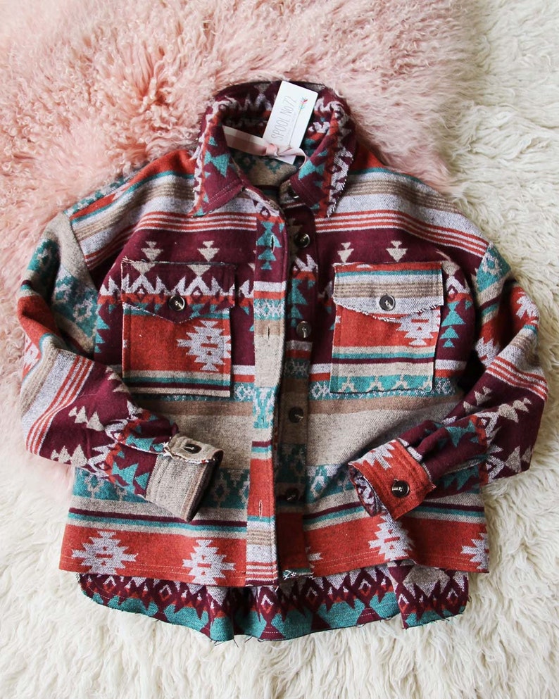 Peut inclure: Une chemise en flanelle &agrave; motif rouge, turquoise et marron avec un devant boutonn&eacute; et des manches longues. La chemise a un design d'inspiration sud-ouest.