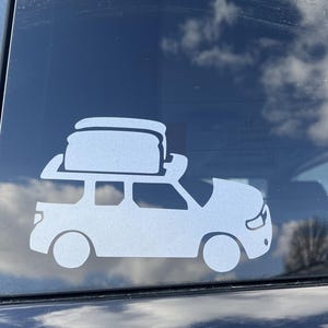 May include: A white silhouette of a car with a roof rack and two rectangular objects on top. The car is facing the right side of the image. The image is on a dark blue background.