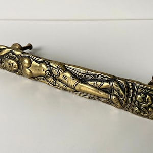 May include: A gold-toned door handle with an ornate design featuring a reclining female figure and floral motifs.