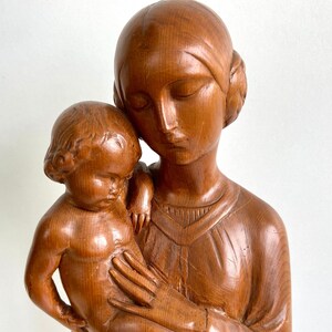 Puede incluir: Una escultura de madera de una madre y un niño. La madre está sosteniendo al niño en sus brazos. Ambas figuras están talladas en un estilo realista y tienen un color cálido y marrón.