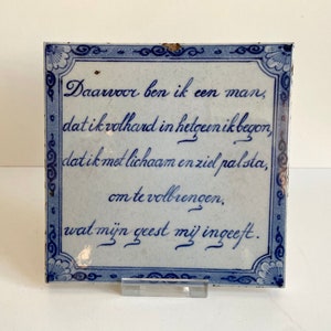 Puede incluir: Un azulejo de Delft azul y blanco con un proverbio holandés en escritura azul: "Daarvoor ben ik een man, dat ik volhard in hetgeen ik begon, dat ik met lichaam en ziel pal sta, om te volbrengen, wat mijn geest mij ingeeft."