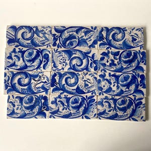 May include: A collection of rectangular ceramic tiles with a white background and a blue floral design. The design features swirling patterns, flowers, and leaves. The tiles are arranged in a grid.