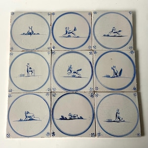 Può includere: Nove piastrelle quadrate in ceramica con illustrazioni di animali blu su sfondo bianco. Ogni piastrella presenta un animale diverso, come un coniglio, un cervo o una volpe, all'interno di un cerchio blu. Disposizione a griglia 3x3, stile vintage.