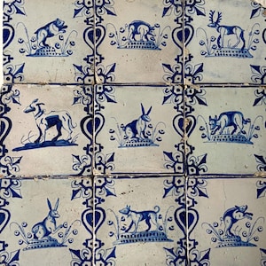 Puede incluir: Conjunto de baldosas cerámicas cuadradas con ilustraciones azules sobre fondo blanco. Cada baldosa presenta un animal diferente, como un perro, un conejo y un ciervo, rodeado de motivos florales. Las baldosas están dispuestas juntas.