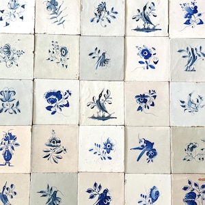 Puede incluir: Una colección de azulejos de cerámica cuadrados dispuestos en cuadrícula, cada uno con ilustraciones en tinta azul pintadas a mano sobre un fondo blanco roto o gris claro. Los diseños representan diversos motivos florales y aves.