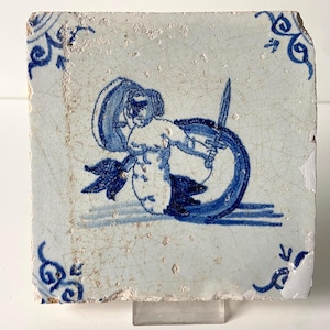 Puede incluir: Un azulejo de Delft azul y blanco que representa una figura sosteniendo una espada, con un diseño floral en el fondo.