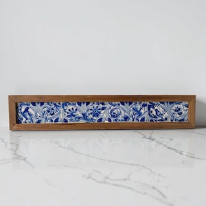 May include: A rectangular wooden frame holds five ceramic tiles. Each tile features a blue and white floral and bird design. The frame is made of light brown wood, and the tiles are arranged horizontally.