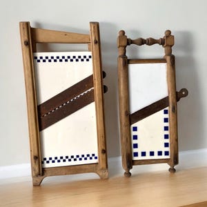 May include: Two antique wooden food slicers with blue and white checkered tile insets. The slicers have a wooden frame and a metal blade.