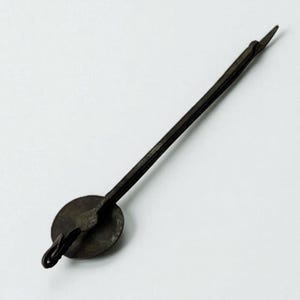 May include: A dark, antique-style metal clock pendulum. The pendulum features a circular disc, a long, slender rod, and a pointed tip. The metal has a weathered appearance, suggesting age or a vintage aesthetic. The design is simple and functional.