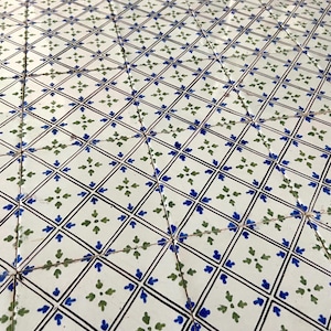 Puede incluir: Una superficie de baldosas con un patrón repetitivo de cuadrados blancos delineados en negro. Cada cuadrado contiene un patrón de diamante más pequeño con motivos florales azules y verdes. Las baldosas están dispuestas en diagonal.