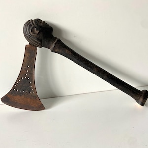 May include: A wooden axe with a carved human head on the handle. The axe head is made of metal and has a decorative pattern of holes.