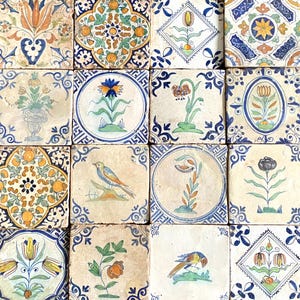 May include: A collection of sixteen antique ceramic tiles. Each square tile features a unique hand-painted design, including floral patterns, birds, and geometric shapes. The color palette includes blues, yellows, oranges, and greens, creating a vintage aesthetic.
