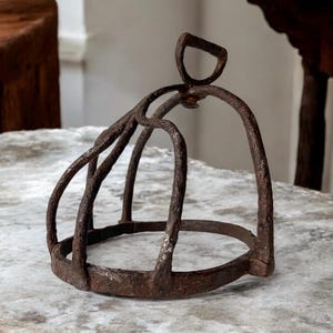 May include: A rusty metal horse bit with a curved top and a circular base. The bit is designed to fit in a horse's mouth and is used to control the horse.