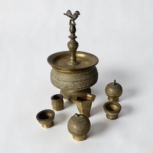 Könnte beinhalten: Eine Sammlung antiker dekorativer Gegenstände aus Messing. Das Set umfasst eine große, verzierte Schale mit einem vogelgekrönten Ständer, mehrere kleine Schalen, einen zylindrischen Behälter und eine Kugel mit Deckel. Die Teile weisen detaillierte geätzte Muster auf.