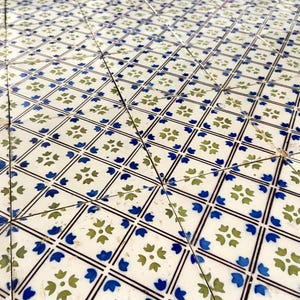 May include: A white tiled floor with a repeating pattern of blue and green floral designs. The tiles are arranged in a diamond pattern.