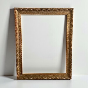 May include: Ornate rectangular picture frame with a gold finish. The frame has detailed embossed patterns along the edges and a white interior. The frame is empty, ready to display a photograph or artwork.