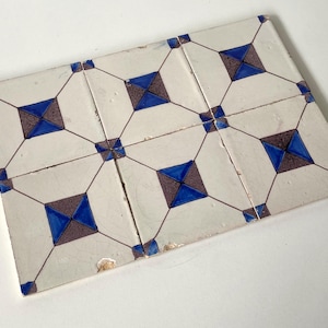 May include: A set of six square ceramic tiles arranged in a grid, featuring a white background with a geometric pattern of dark brown and blue diamond shapes connected by thin brown lines, showing signs of wear and minor surface imperfections.