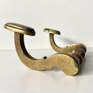 May include: Two antique brass door handles. The handles have a curved design with a decorative, rounded grip. The handles are a warm, aged brass color, with a slightly tarnished appearance, suggesting age and use. The handles are set against a white background.