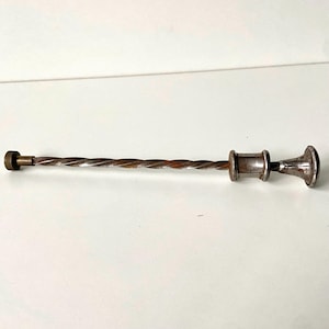 May include: A silver metal tool with a twisted shaft and a decorative handle. The tool has a brass tip.