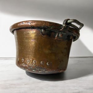 May include: Antique copper pot with a single handle. The pot has a hammered finish and a worn patina.